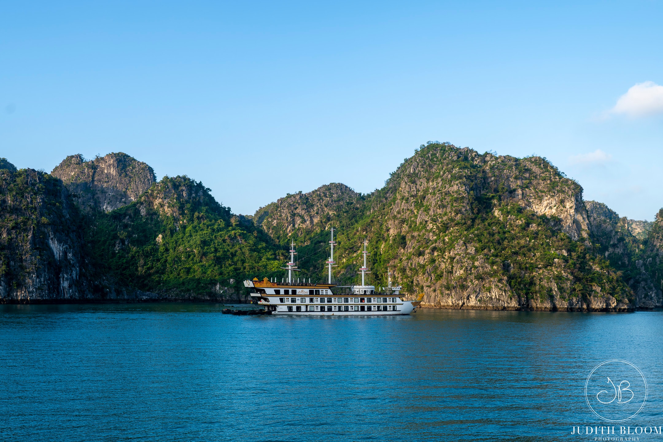 A luxury cruise ship anchored against the dramatic green karst cliffs of Ha Long Bay under a clear blue sky