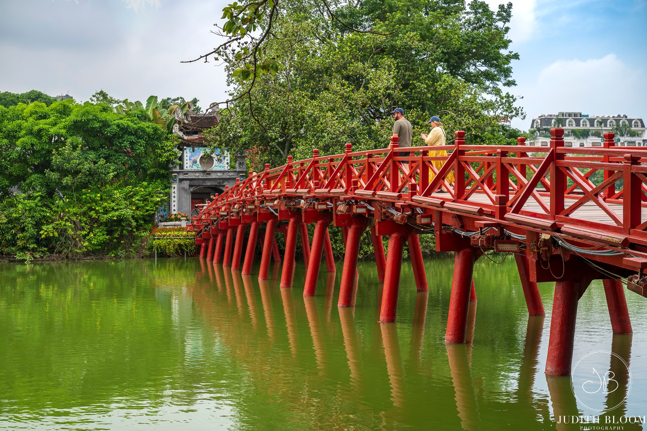 The iconic red Huc Bridge over Hoan Kiem Lake, Hanoi, reflected in green water