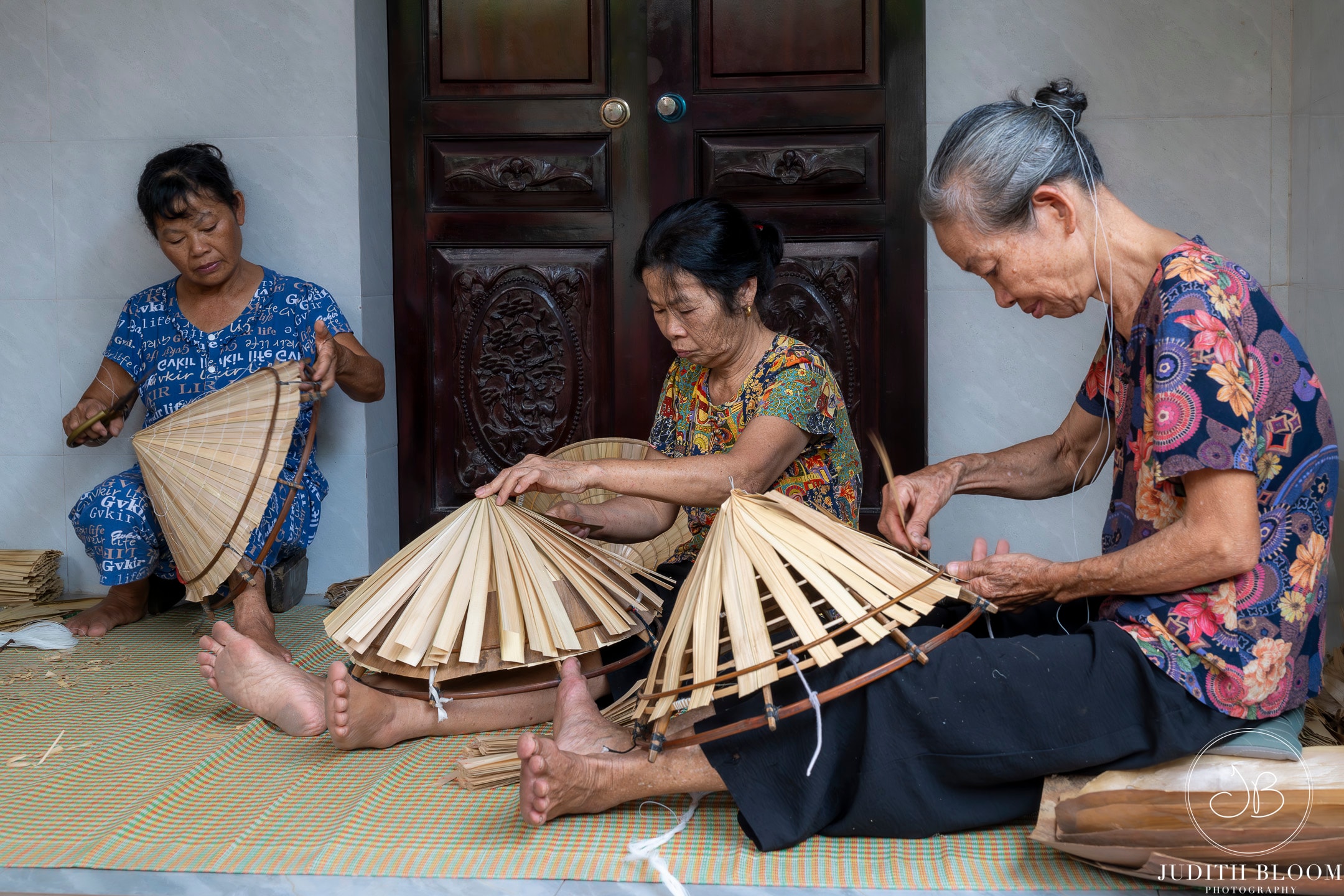 Three women weaving traditional Vietnamese conical hats by hand