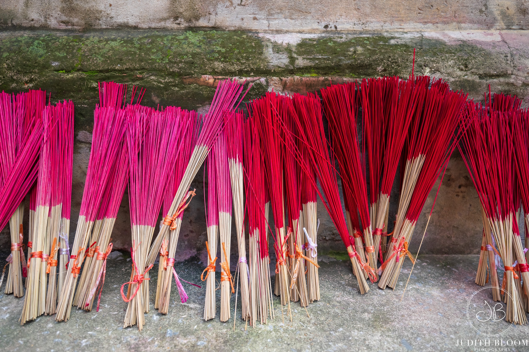Vibrant bundles of pink and red incense sticks drying against a stone wall