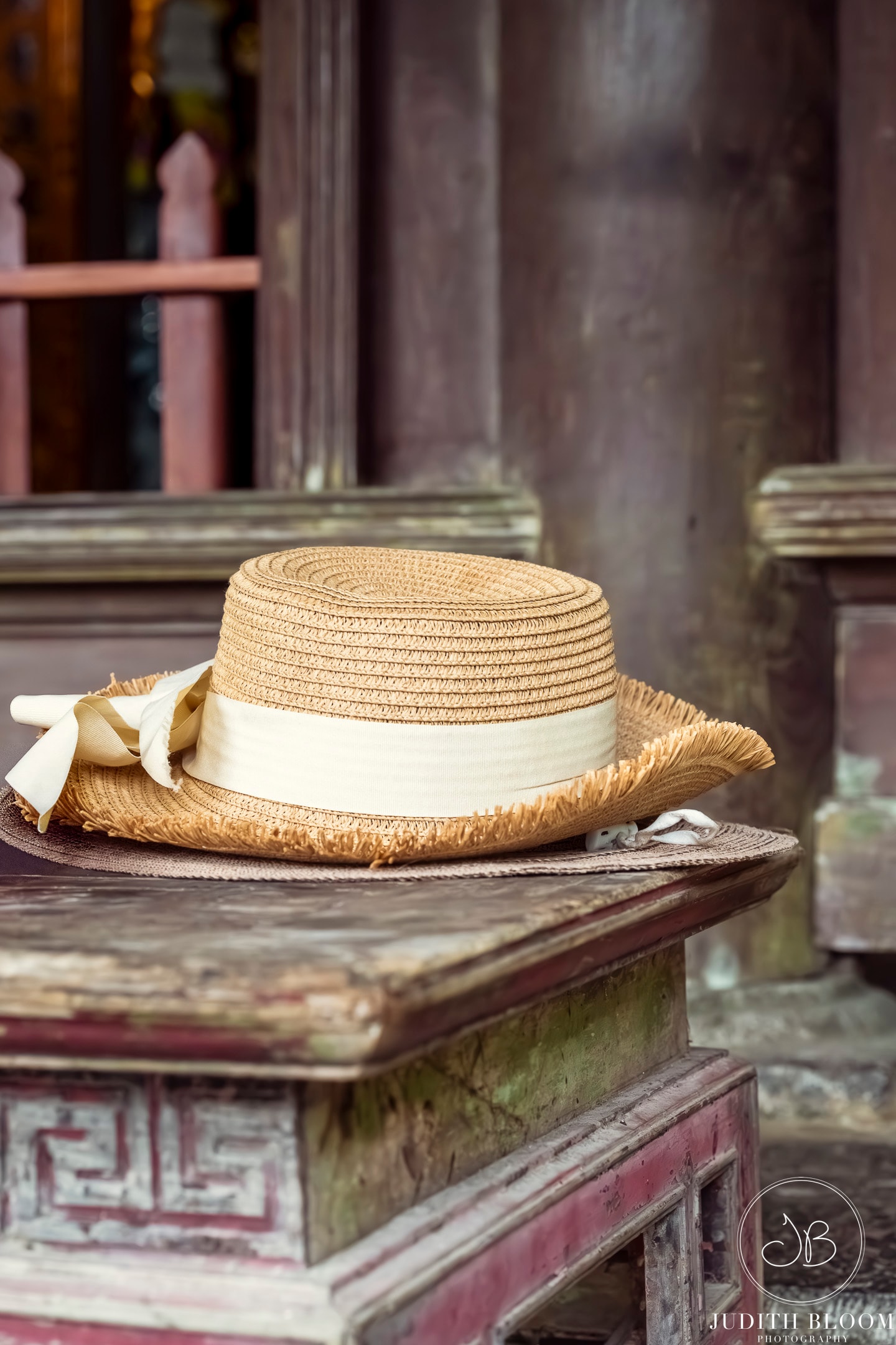 A woven straw hat with cream ribbon rests on the carved steps of a Vietnamese temple