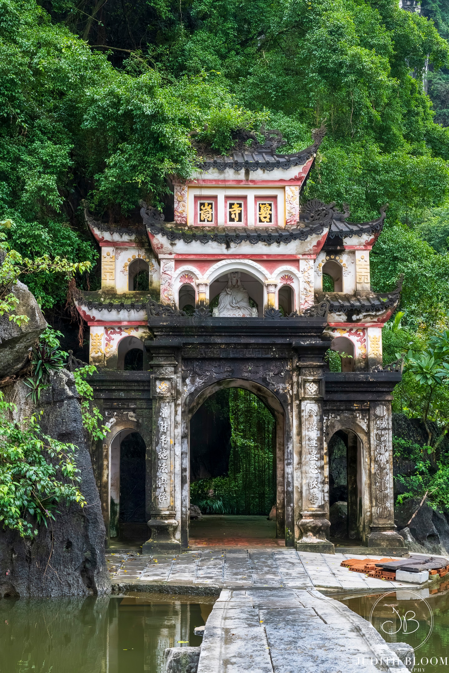 The ornate multi-tiered gateway of Bich Dong Pagoda rises above a stone causeway surrounded by jungle