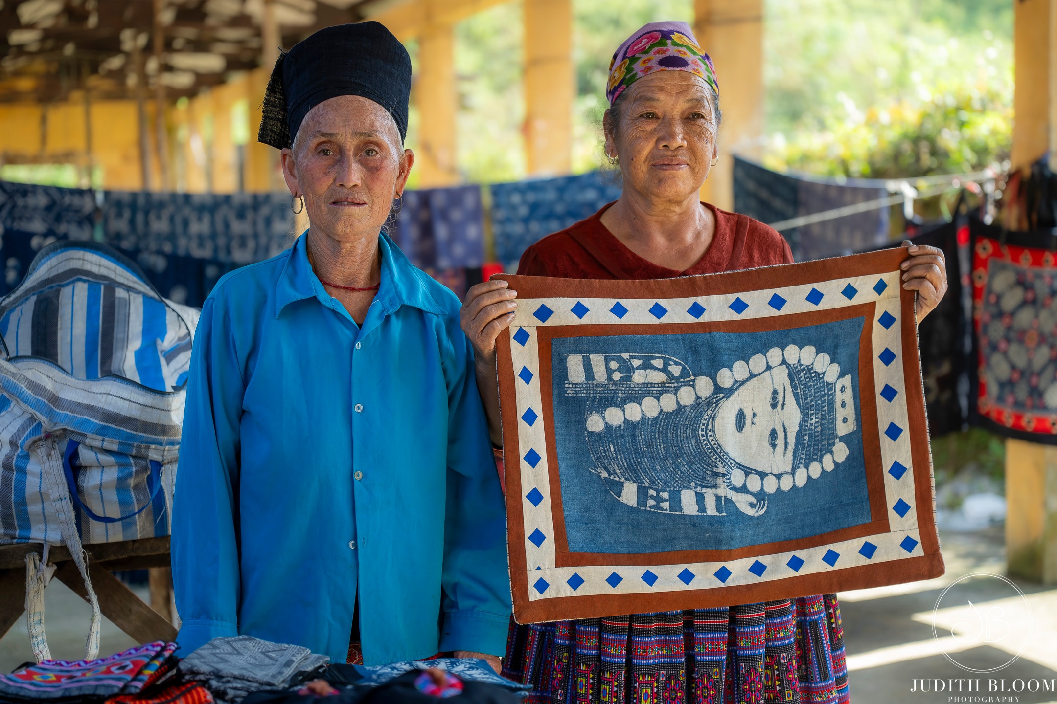 Two artisans proudly display a hand-printed indigo textile at a village market