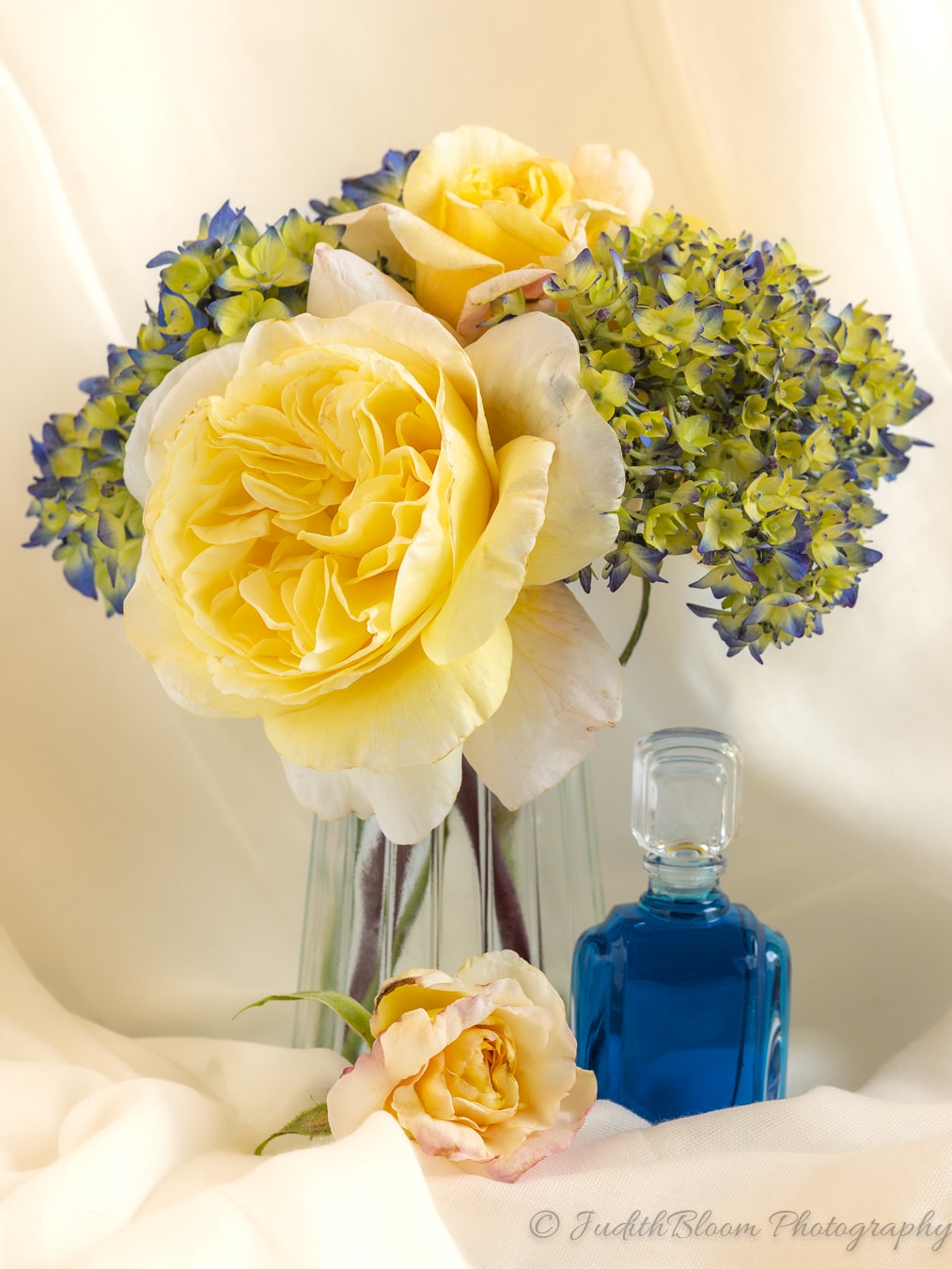 Yellow roses and blue hydrangea in a glass vase with a cobalt blue bottle